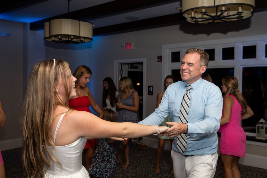 a girl in a white dress holding hands with a man in a blue shirt while dancing in a room.